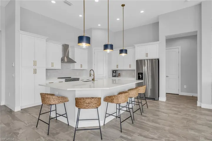 Kitchen with a spacious island, wall chimney range hood, pendant lighting, white cabinetry, and appliances with stainless steel finishes