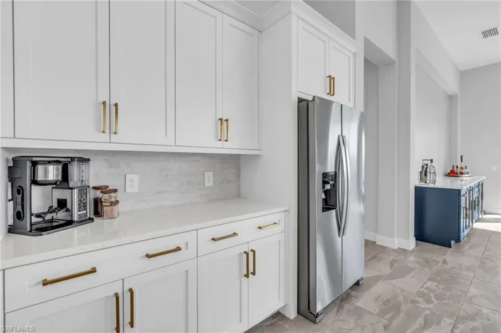 Kitchen with stainless steel fridge with ice dispenser, light stone counters, white cabinets, and tasteful backsplash