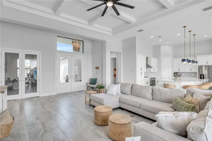Living room with beam ceiling, ceiling fan with notable chandelier, a towering ceiling, french doors, and coffered ceiling