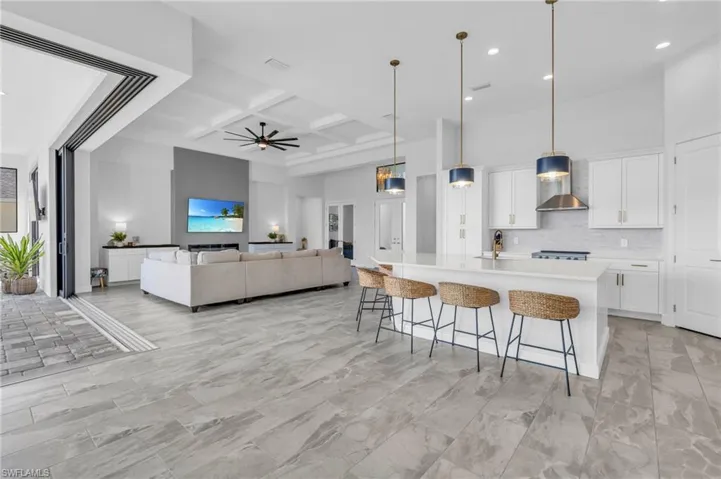 Kitchen featuring a large island with sink, coffered ceiling, wall chimney exhaust hood, pendant lighting, and white cabinetry