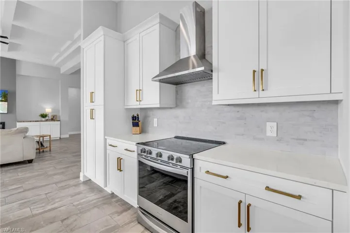 Kitchen with stainless steel range with electric stovetop, decorative backsplash, white cabinetry, and wall chimney range hood
