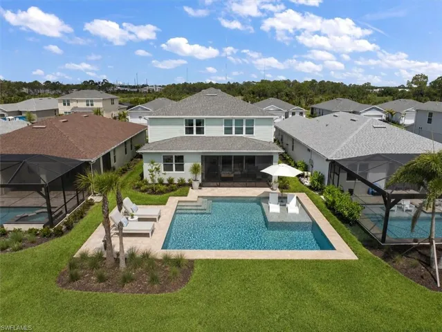 Expansive backyard featuring a rectangular swimming pool with an integrated sun shelf, surrounded by light-toned paver decking
