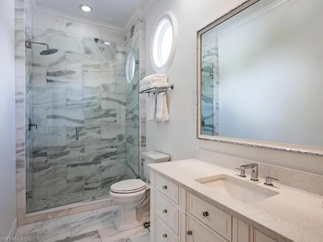 Full bath with vanity, light marble finish flooring, a marble finish shower, and ornamental molding