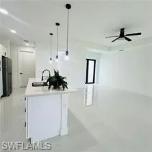 Kitchen featuring a center island with sink, white cabinetry, pendant lighting, freestanding refrigerator, and ceiling fan