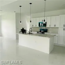 Kitchen featuring white cabinets, a kitchen island with sink, black gas stove, and pendant lighting