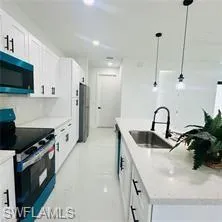 Kitchen with stainless steel appliances, white cabinets, a large island with sink, and pendant lighting