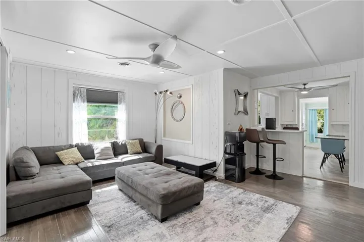 Living room featuring a ceiling fan, dark wood-style flooring, recessed lighting, and wooden walls - Virtually Edited Image
