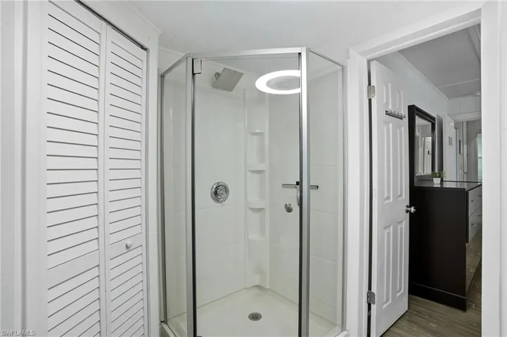 Bathroom featuring a closet, a shower stall, wood finished floors, and ornamental molding - Virtually Edited Image