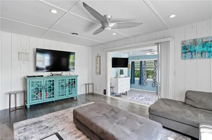 Living room featuring recessed lighting, wood walls, ceiling fan, and wood finished floors - Virtually Edited Image