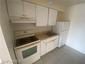 Kitchen featuring white appliances, white cabinetry, under cabinet range hood, and light countertops