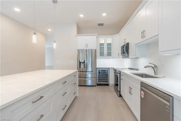 Kitchen featuring stainless steel appliances, wine cooler, pendant lighting, white cabinets, decorative backsplash