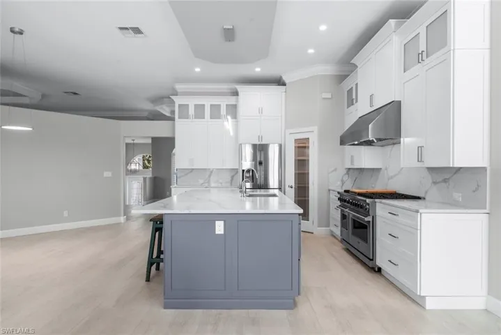 Modern kitchen featuring a large central island with a contrasting base, white shaker-style cabinetry, stainless steel appliances, marble-look countertops and backsplash, and recessed lighting