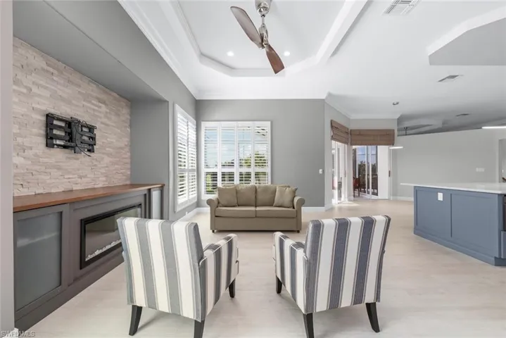 Spacious living area featuring light wood-finish flooring, a tray ceiling with recessed lighting and a ceiling fan, and a built-in media console with an electric fireplace