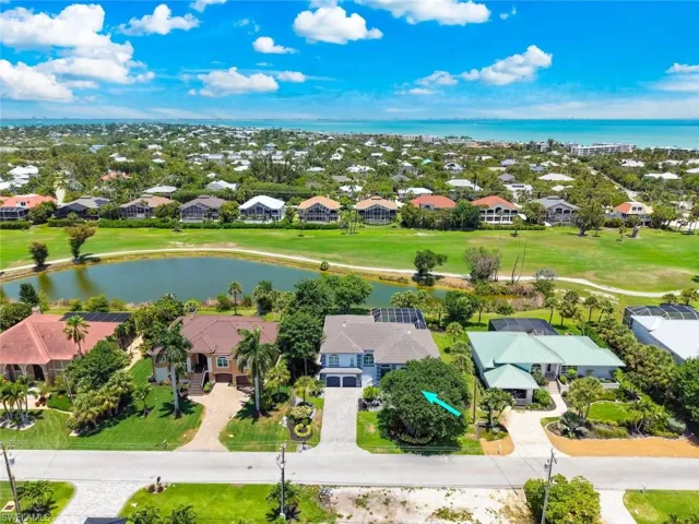 Aerial perspective showcasing a light-colored two-story residence with an attached garage, paver driveway, and mature landscaping