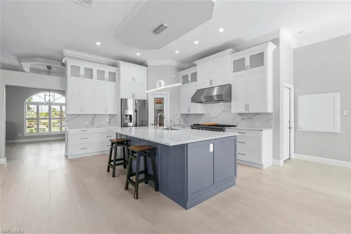 Contemporary kitchen featuring a large central island, light wood-finish flooring, white upper and lower cabinetry, stainless steel appliances, and a tray ceiling