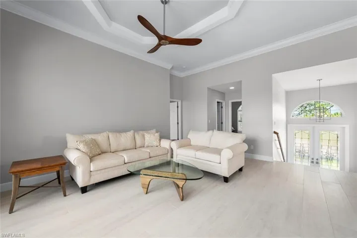 Spacious living area featuring light-toned wood-finish flooring and a tray ceiling with a ceiling fan