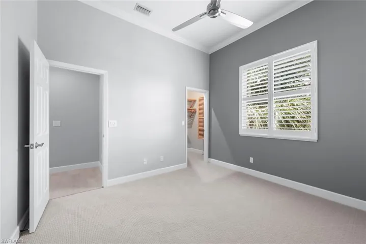 Spacious room featuring neutral carpeting, a modern ceiling fan, and a window with plantation shutters