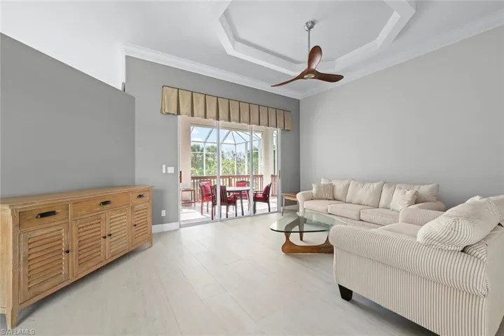 Spacious living area featuring light wood-finish flooring, a contemporary ceiling fan, and a tray ceiling