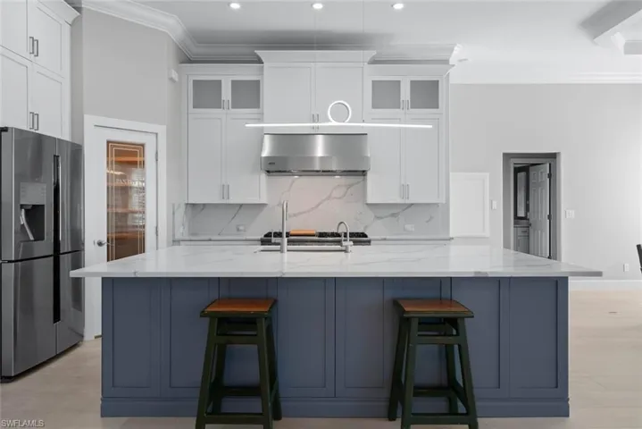 Gourmet kitchen featuring a large central island with a quartz countertop, stainless steel appliances, white cabinetry with glass inserts, and a decorative pendant light fixture