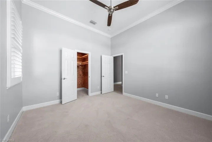Carpeted interior room featuring a ceiling fan, crown molding, plantation shutters, and a walk-in closet with built-in shelving