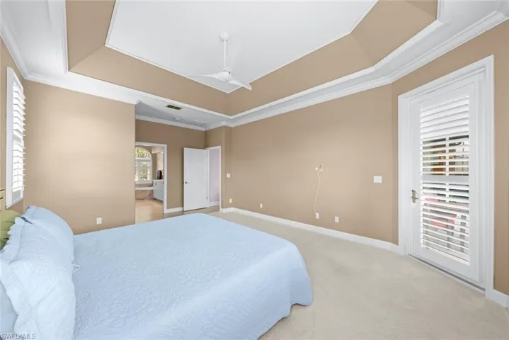 Carpeted interior space featuring a tray ceiling with crown molding, a ceiling fan, and plantation shutters on the window and door