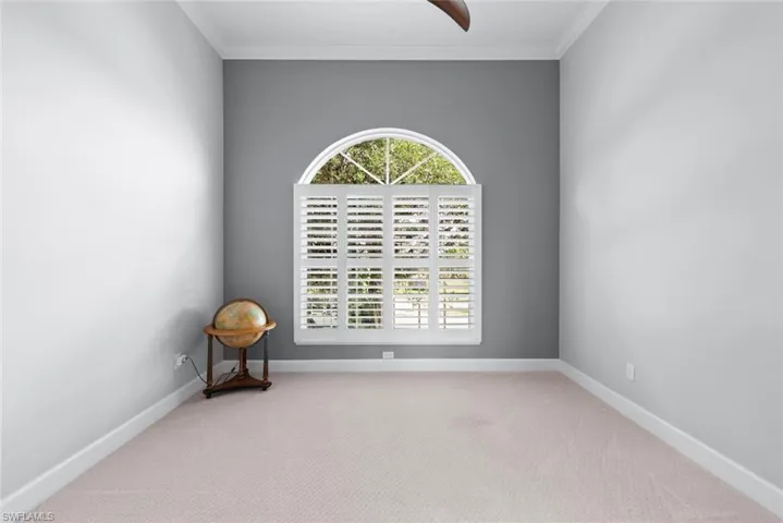 Room featuring an arched window with plantation shutters, light-colored carpeting, a ceiling fan, and crown molding