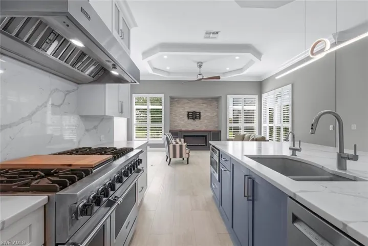 Gourmet kitchen featuring a stainless steel range with a professional-grade hood, white cabinetry, and a large central island with a double sink