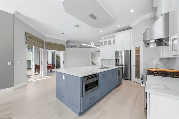 Spacious kitchen featuring an expansive central island with a built-in microwave, light wood-finish flooring, white upper cabinetry, stainless steel appliances, and quartz countertops with a matching backsplash