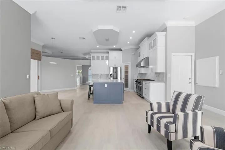 Open-concept living area featuring light wood-finish flooring, recessed lighting, and crown molding