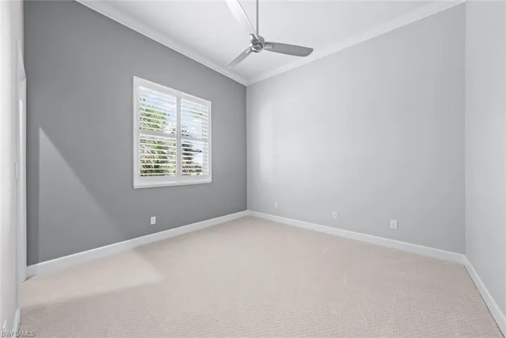 Room featuring a window with white louvered shutters, light gray painted walls, textured carpeting, white baseboards, and a ceiling fan