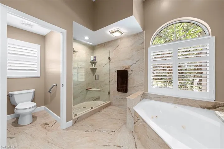 Spacious bathroom featuring a soaking tub, a separate glass-enclosed shower, and stone-finish tile flooring