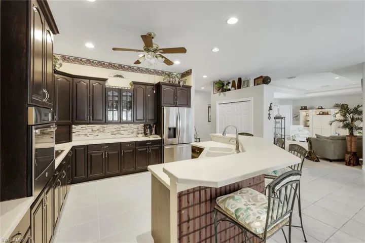 Kitchen featuring glass fronted cabinets, stainless steel appliances, a kitchen breakfast bar, a ceiling fan, and an island with sink