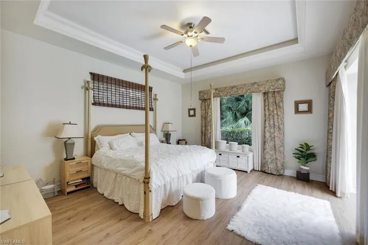 Bedroom with a tray ceiling, light wood-type flooring, and a ceiling fan