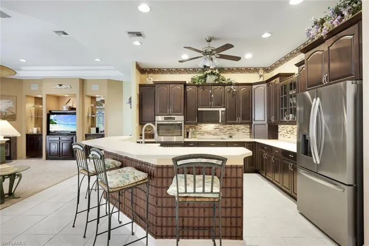 Kitchen featuring stainless steel appliances, a kitchen bar, glass insert cabinets, dark wood finish cabinetry, and a center island with sink