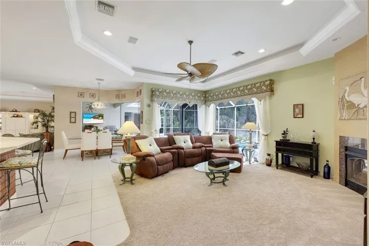 Living area featuring a glass covered fireplace, a tray ceiling, light carpet, ceiling fan, and light tile patterned floors