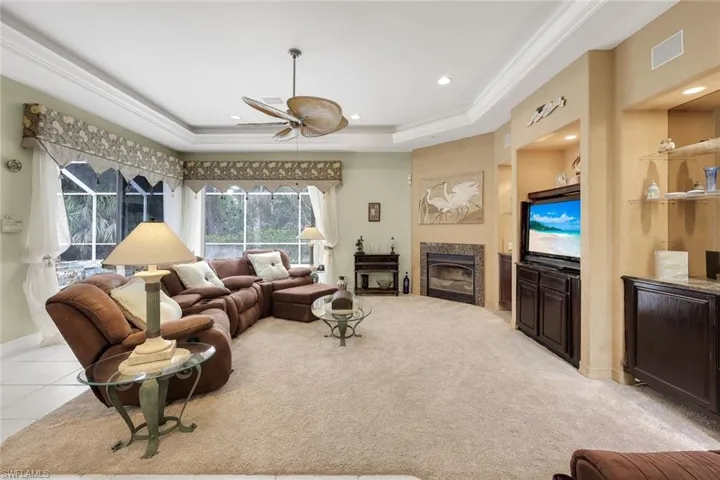 Living area with a fireplace, ceiling fan, a raised ceiling, light carpet, and recessed lighting