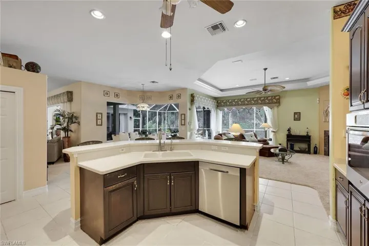 Kitchen featuring dark wood finish cabinets, stainless steel appliances, open floor plan, ceiling fan, and an island with sink