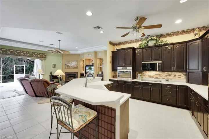 Kitchen with ceiling fan, a breakfast bar, a fireplace, dark wood finish cabinetry, and stainless steel appliances