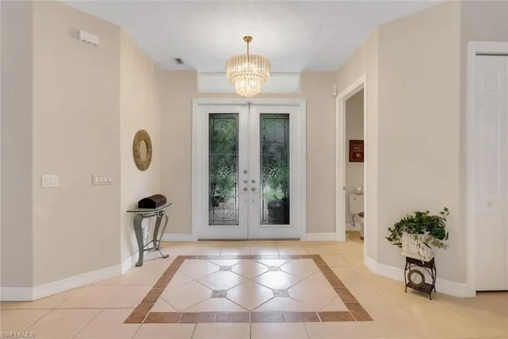 Foyer featuring inlaid floor details, suspended lighting, french doors, and light tile patterned flooring