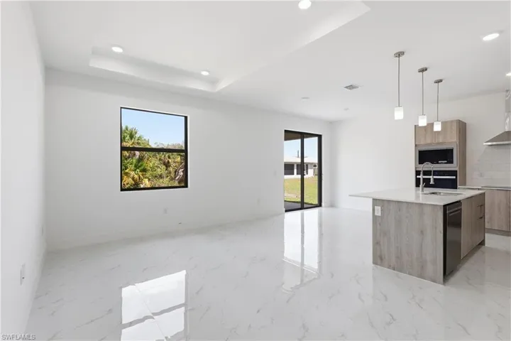 Kitchen with modern cabinets, light stone countertops, a center island with sink, pendant lighting, and a raised ceiling