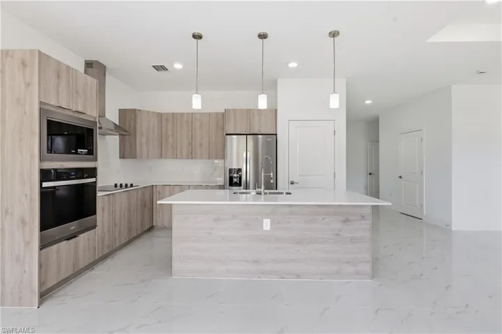 Kitchen featuring modern cabinets, an island with sink, stainless steel appliances, hanging light fixtures, and light stone counters