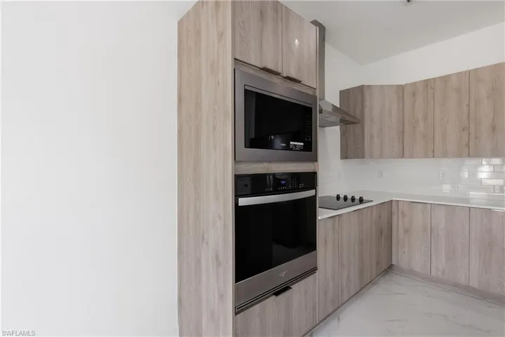Kitchen featuring modern cabinets, oven, built in microwave, and light marble finish flooring