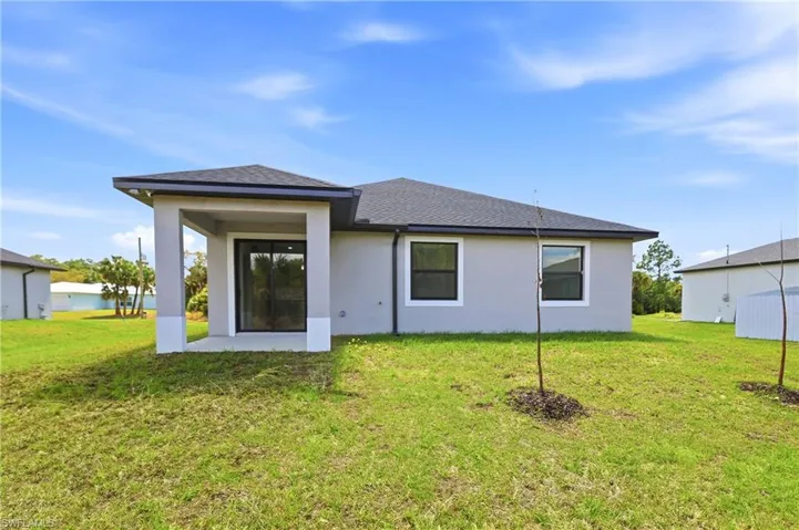 Rear view of property featuring a shingled roof, stucco siding, a yard, and a patio