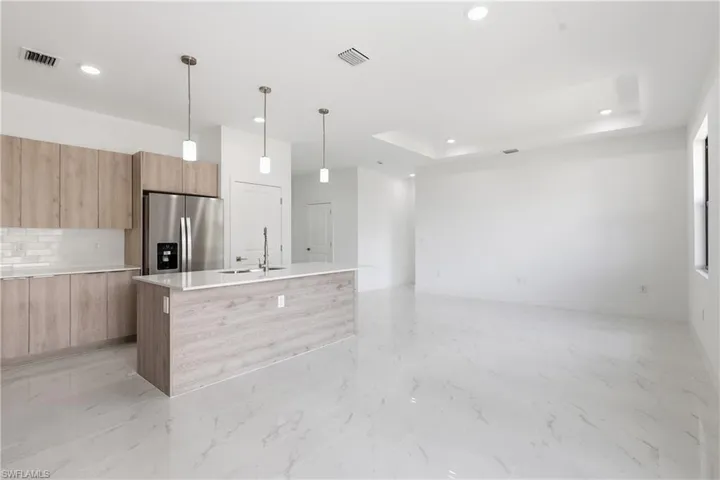 Kitchen with modern cabinets, a kitchen island with sink, stainless steel fridge, light wood finish cabinets, and a raised ceiling