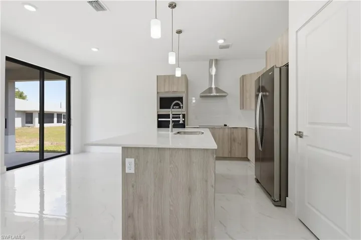 Kitchen featuring modern cabinets, light wood finish cabinets, light marble finish floors, light stone counters, and freestanding refrigerator