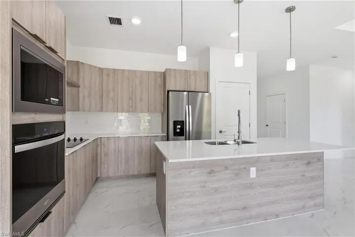 Kitchen with modern cabinets, a kitchen island with sink, light wood finish cabinetry, stainless steel appliances, and light stone counters