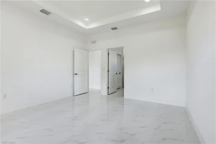 Bedroom featuring a raised ceiling, recessed lighting, and light marble finish floors