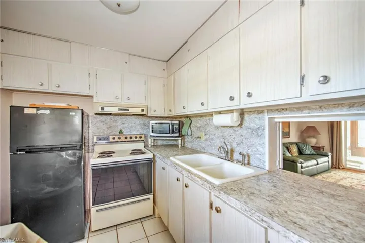 Kitchen featuring sink, white electric range oven, black refrigerator, light tile patterned floors, and exhaust hood