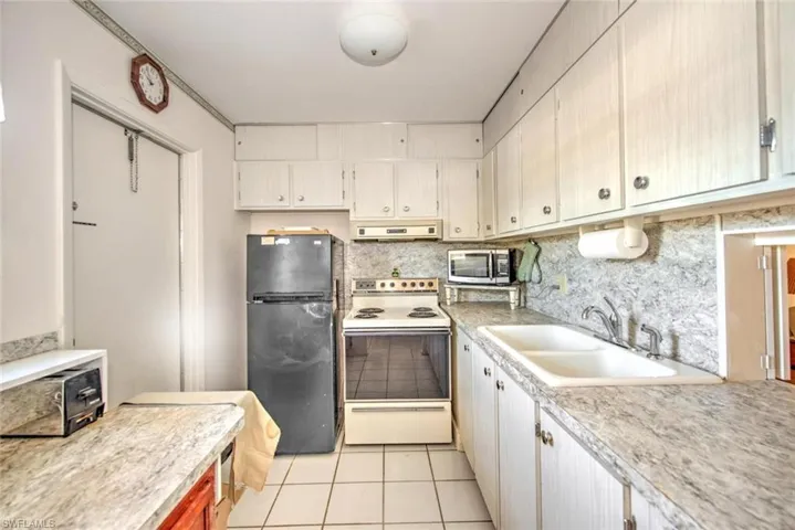 Kitchen featuring sink, black fridge, range hood, white electric stove, and light tile patterned flooring
