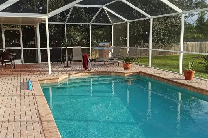 View of pool featuring a patio, glass enclosure, and area for grilling